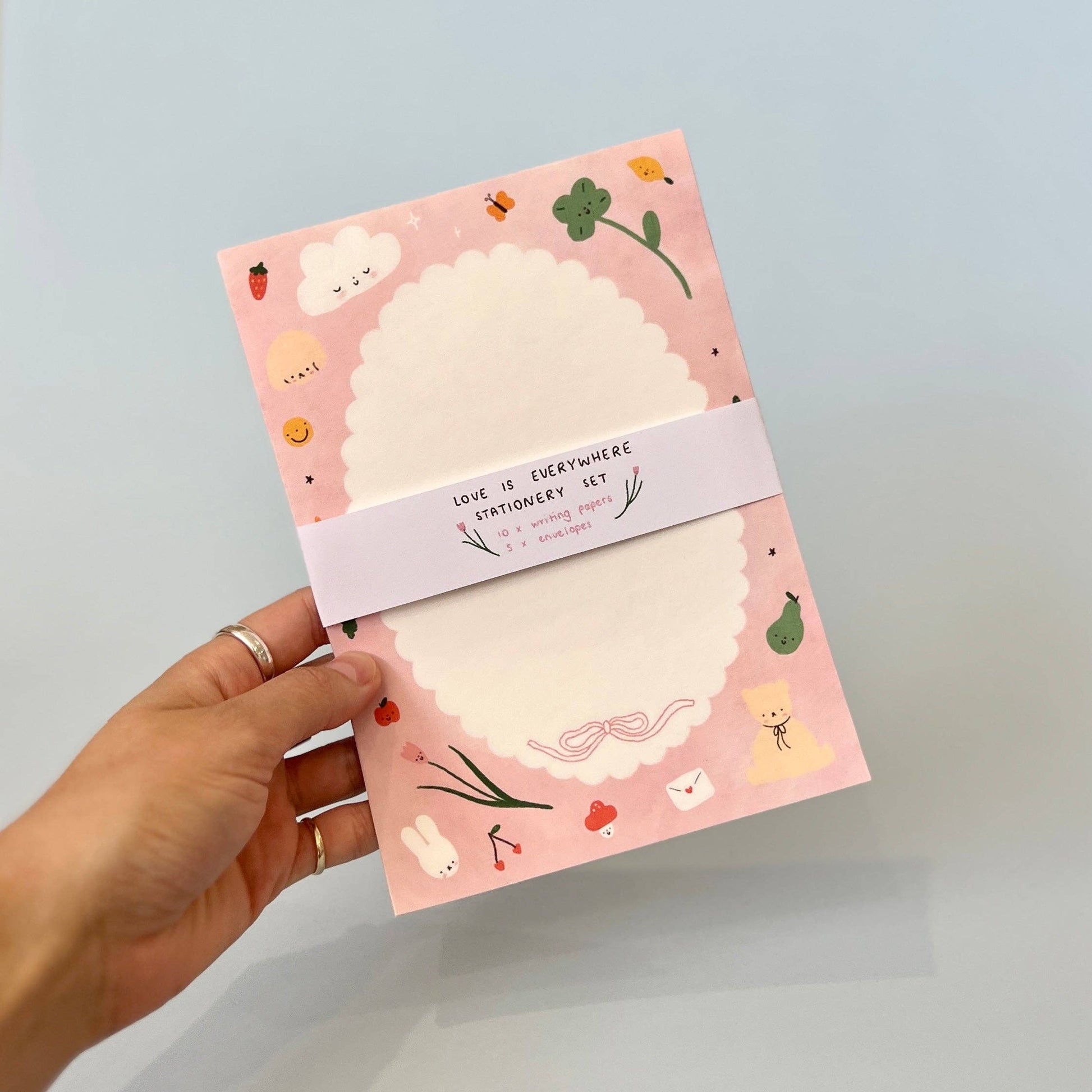 Hand holding a pink stationery set with illustrations on a light blue background