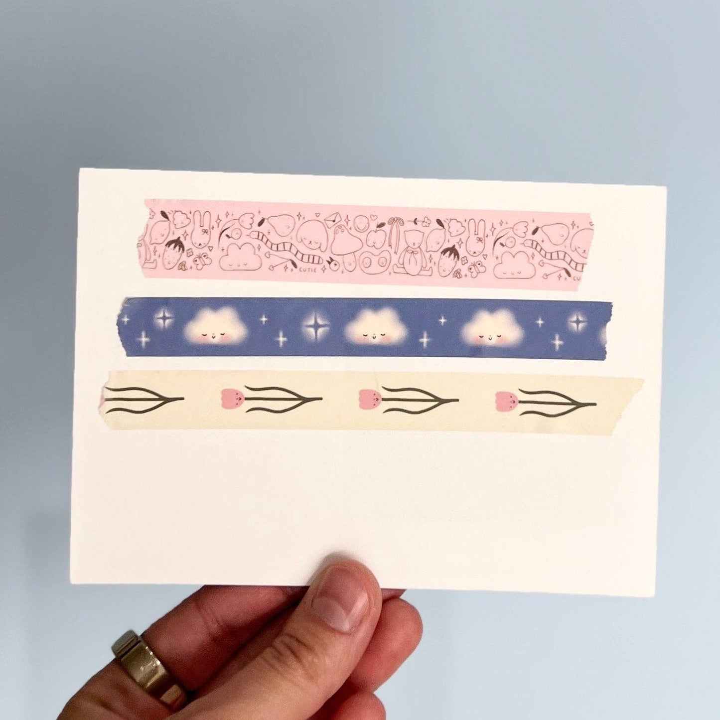 Set of decorative washi tape strips held by a hand on a light blue background
