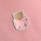 Sticker of a bear holding a book titled 'How to Slay' on a pink background
