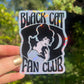 Sticker with 'Black Cat Fan Club' design held in front of green foliage