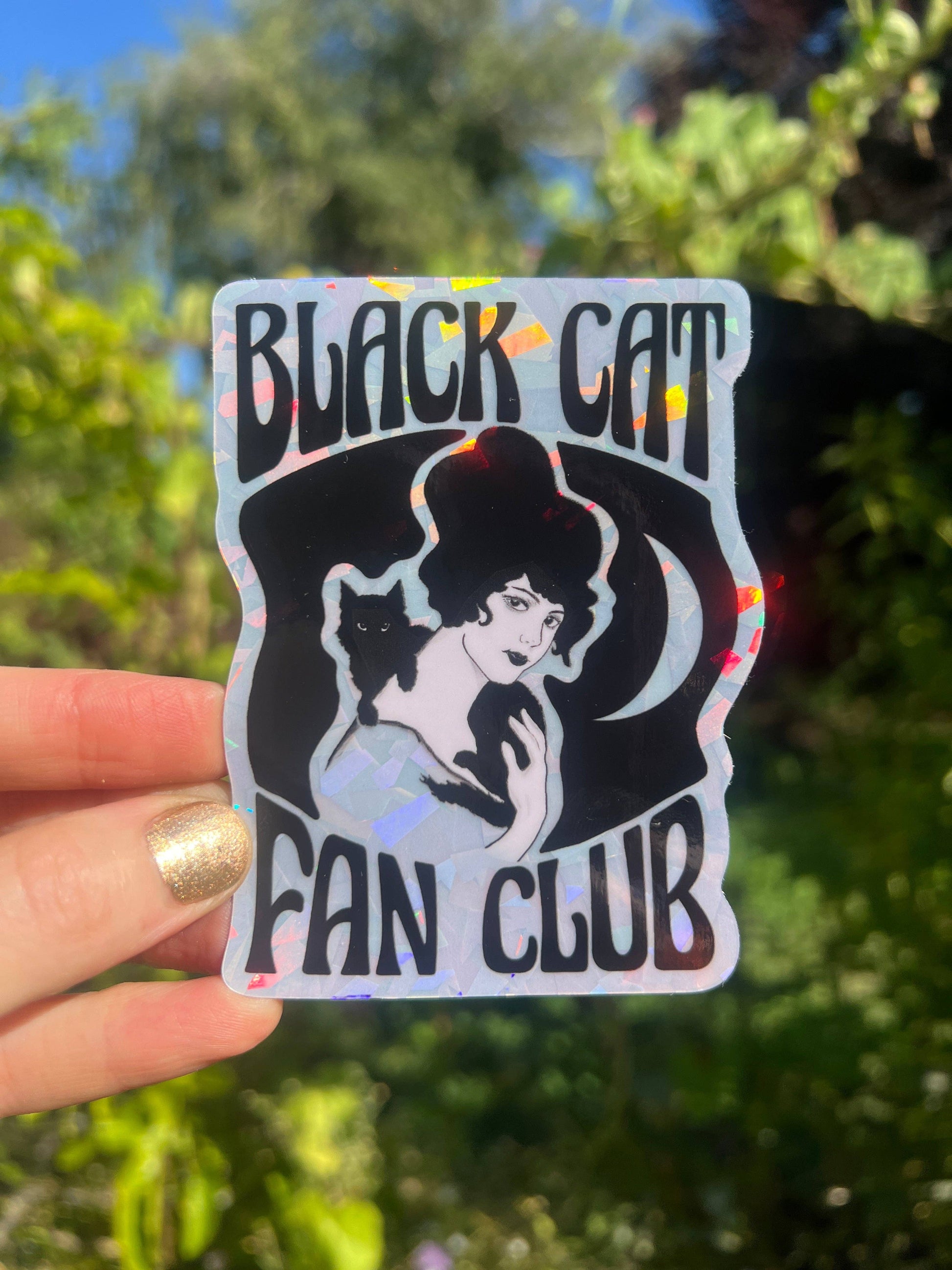 Sticker with 'Black Cat Fan Club' design held in front of green foliage