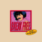 A sticker featuring a person with dark hair and a mustache against a pink patterned background, with large red text reading 'BREAK FREE.' A yellow oval badge in the lower right says 'WOW! Holographic!' on a plain beige background.