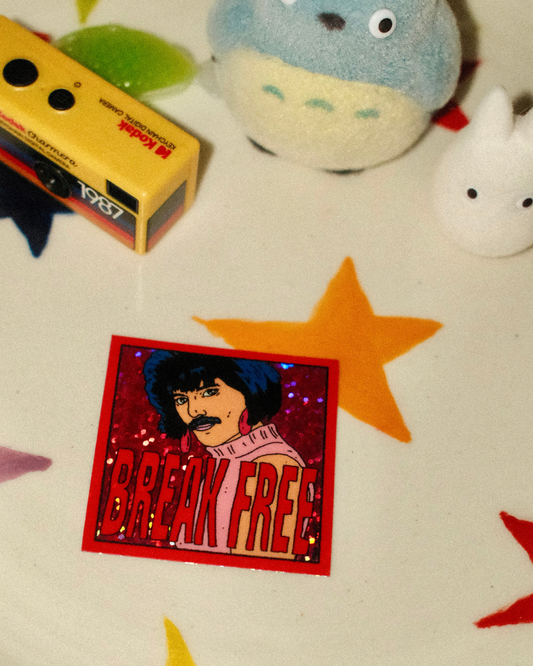 A square sticker  with the words 'BREAK FREE' in large red letters, placed on a white surface with star-shaped cutouts and small plush toys nearby.