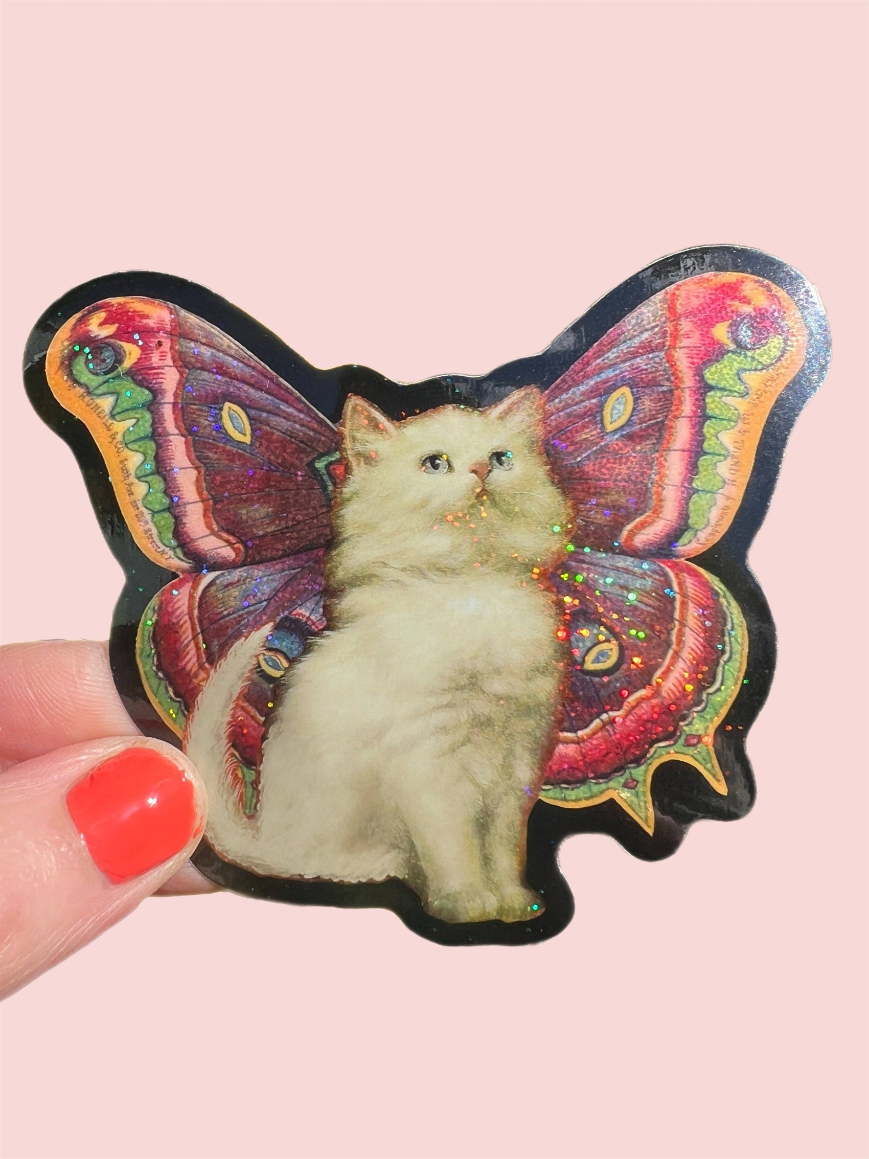 Sticker of a cat with butterfly wings held by a hand on a pink background