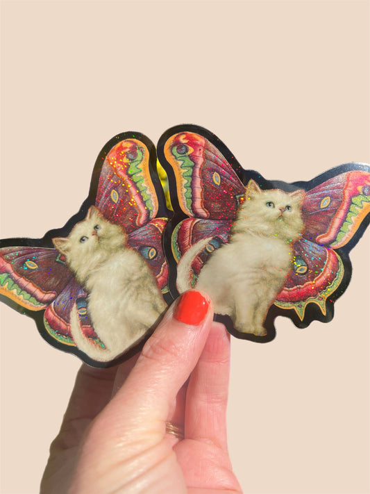 Butterfly-shaped sticker with a cat design held by a hand against a beige background