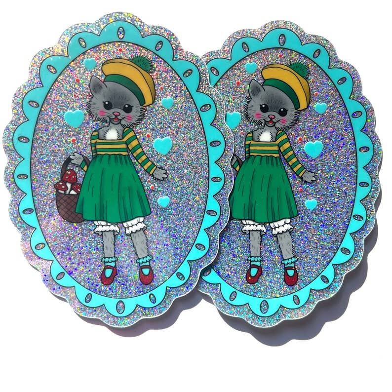 Two identical colorful illustrations of a cat character in a green dress with a blue border on a white background.