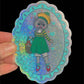 Sticker of a cat in a green dress with a colorful hat held against a black background