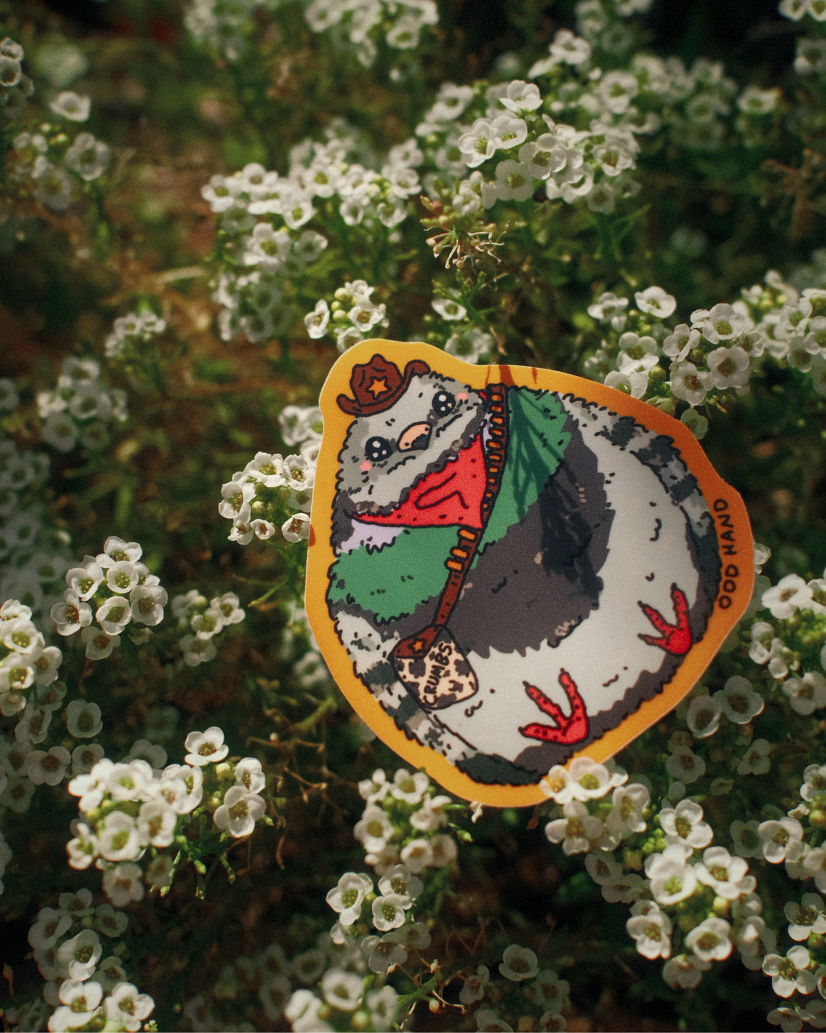 A die-cut sticker featuring a cartoon pigeon wearing a red bandana and green jacket, placed on a bed of small white flowers. The sticker has a yellow border and the text 'OOD OTOO' printed on the right side.