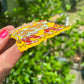 Hand holding a colorful magnet on t he side with a cartoon character against a blurred green outdoor background