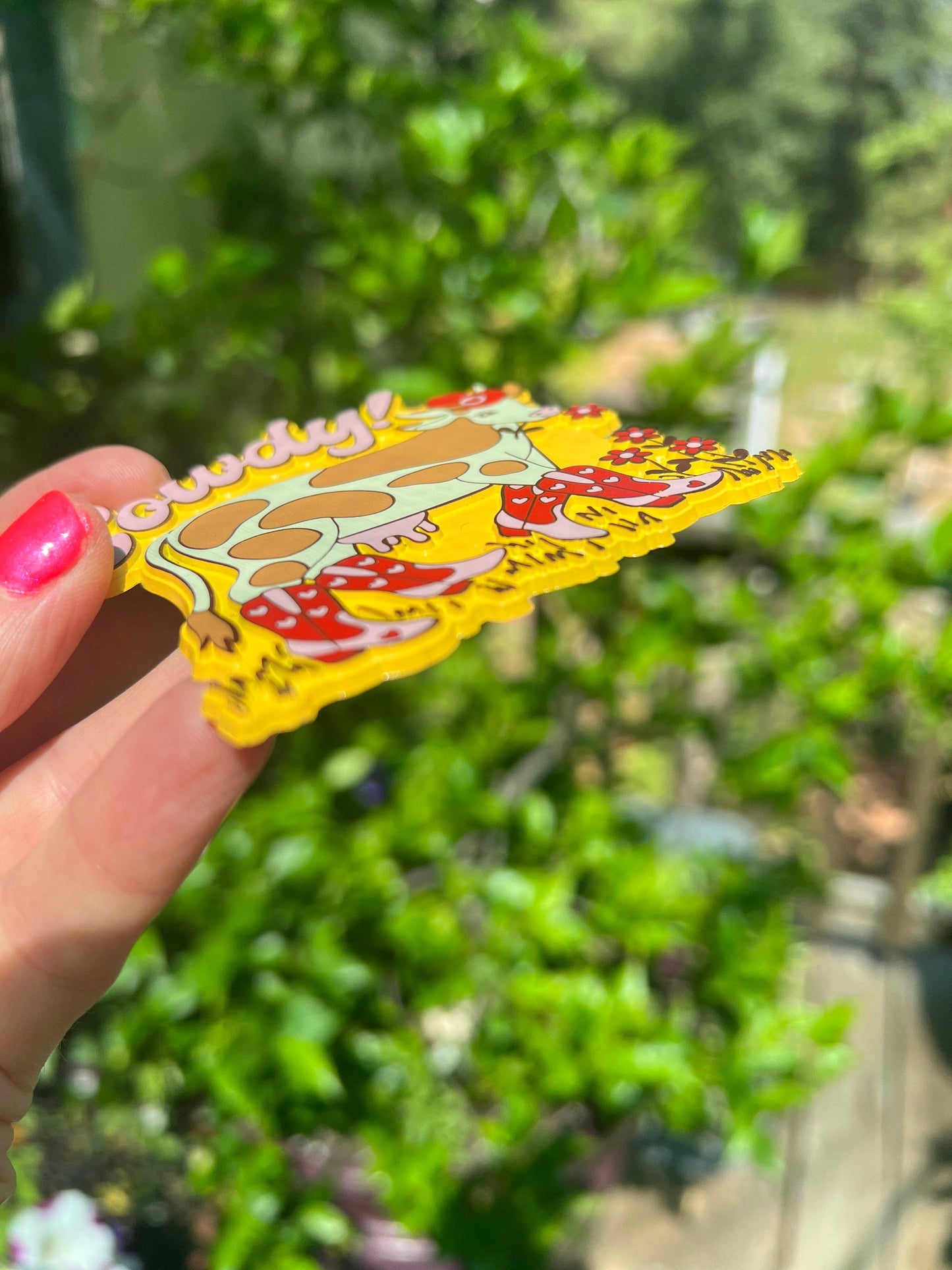Hand holding a colorful magnet on t he side with a cartoon character against a blurred green outdoor background