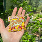 Hand holding a colorful cow magnet  with a blurred green outdoor background