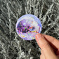 Hand holding a disco ball sticker in front of a bush