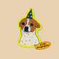 A die-cut holographic sticker or patch featuring a cartoon dog face with brown and white fur, wearing a blue wizard hat with yellow stars, on a beige background. A yellow oval callout reads 'WOW! Holographic!'.