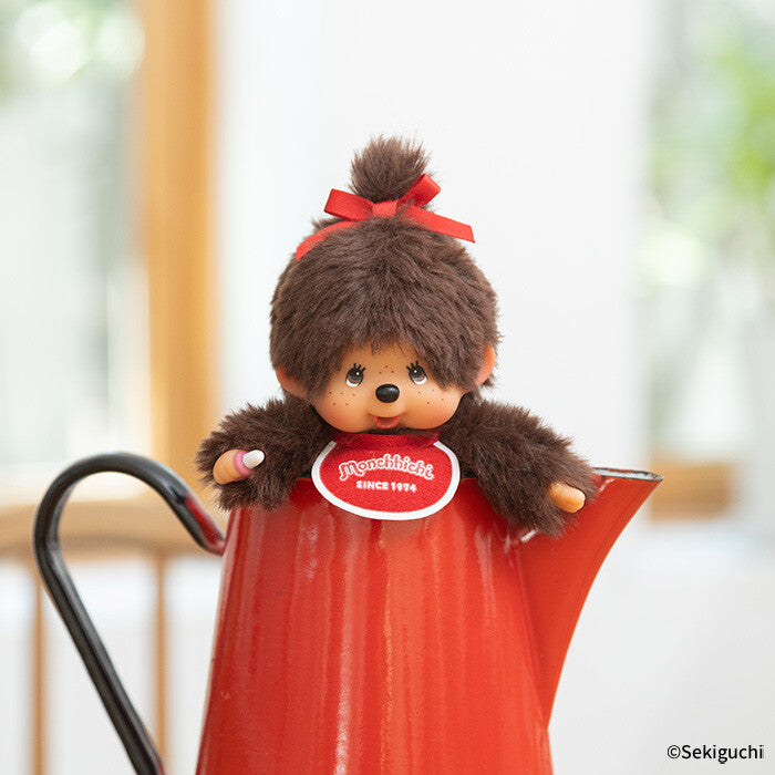 Plush Monchhichi with a red bow on top of its head, sitting inside a red teapot.