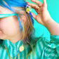 Person with blue hair using a hair clip against a green background