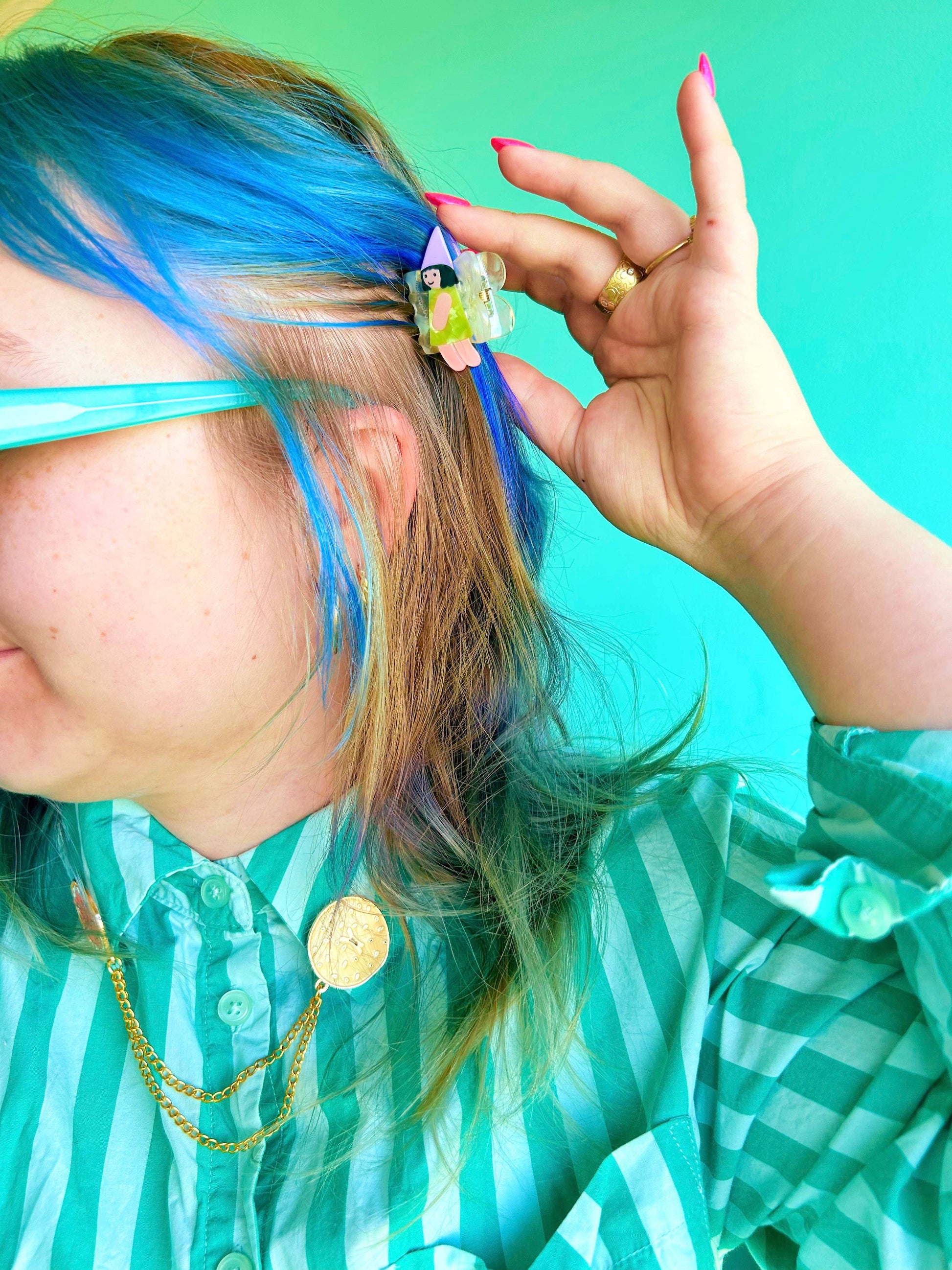 Person with blue hair using a hair clip against a green background