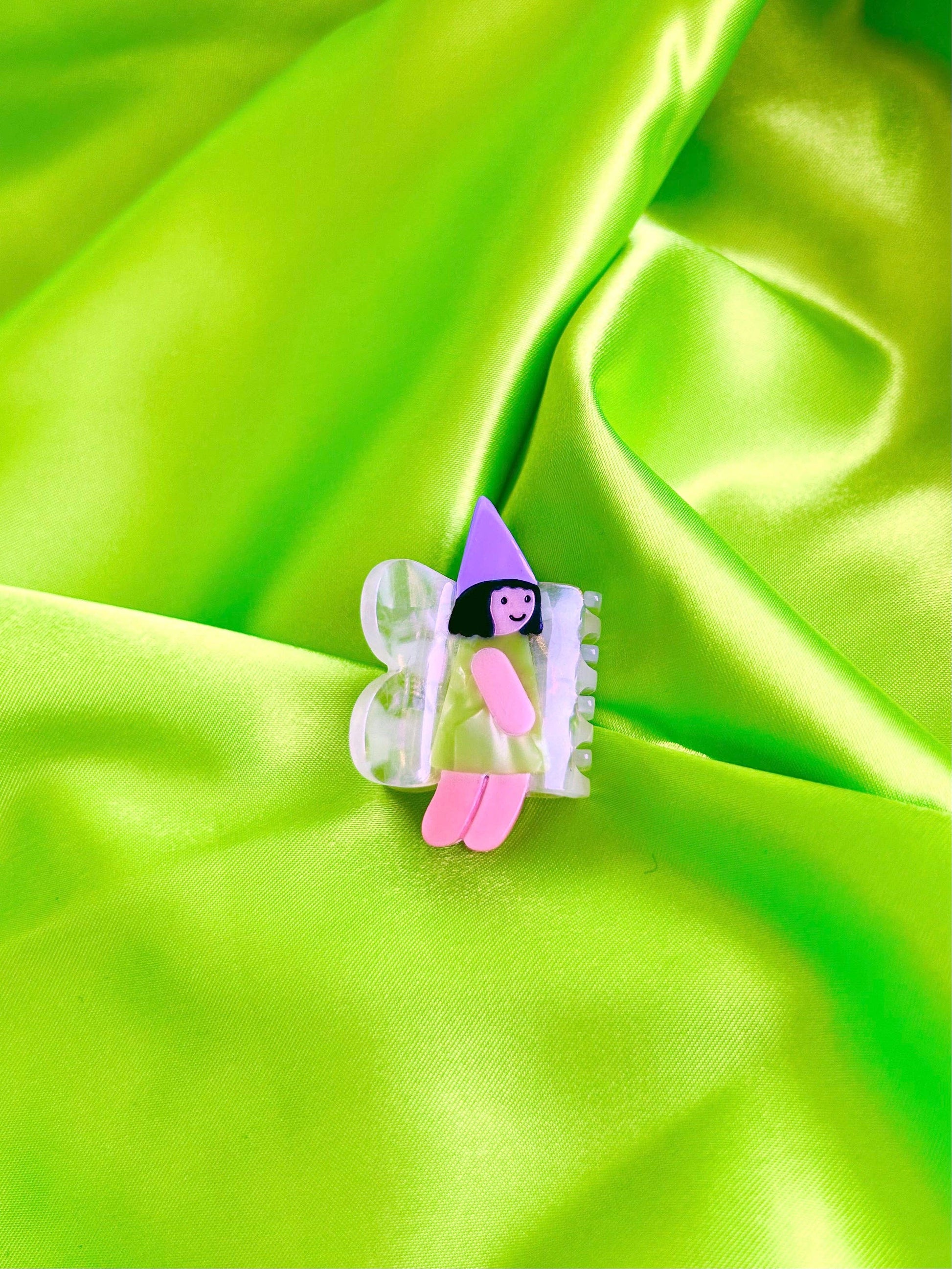 Butterfly-shaped hair clip with a fairy design on a green fabric background
