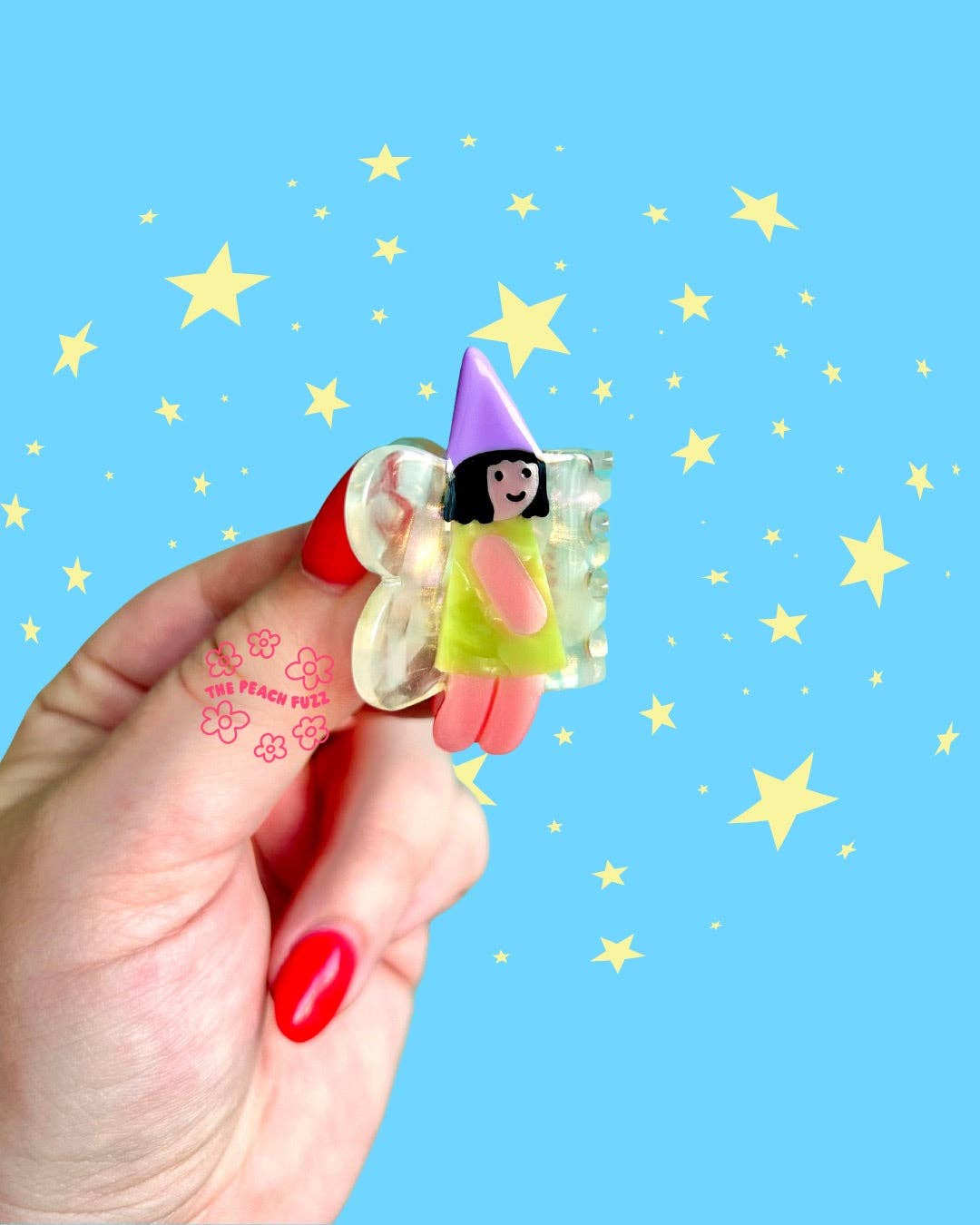 Hand holding a small fairy hair clip against a blue background with yellow stars