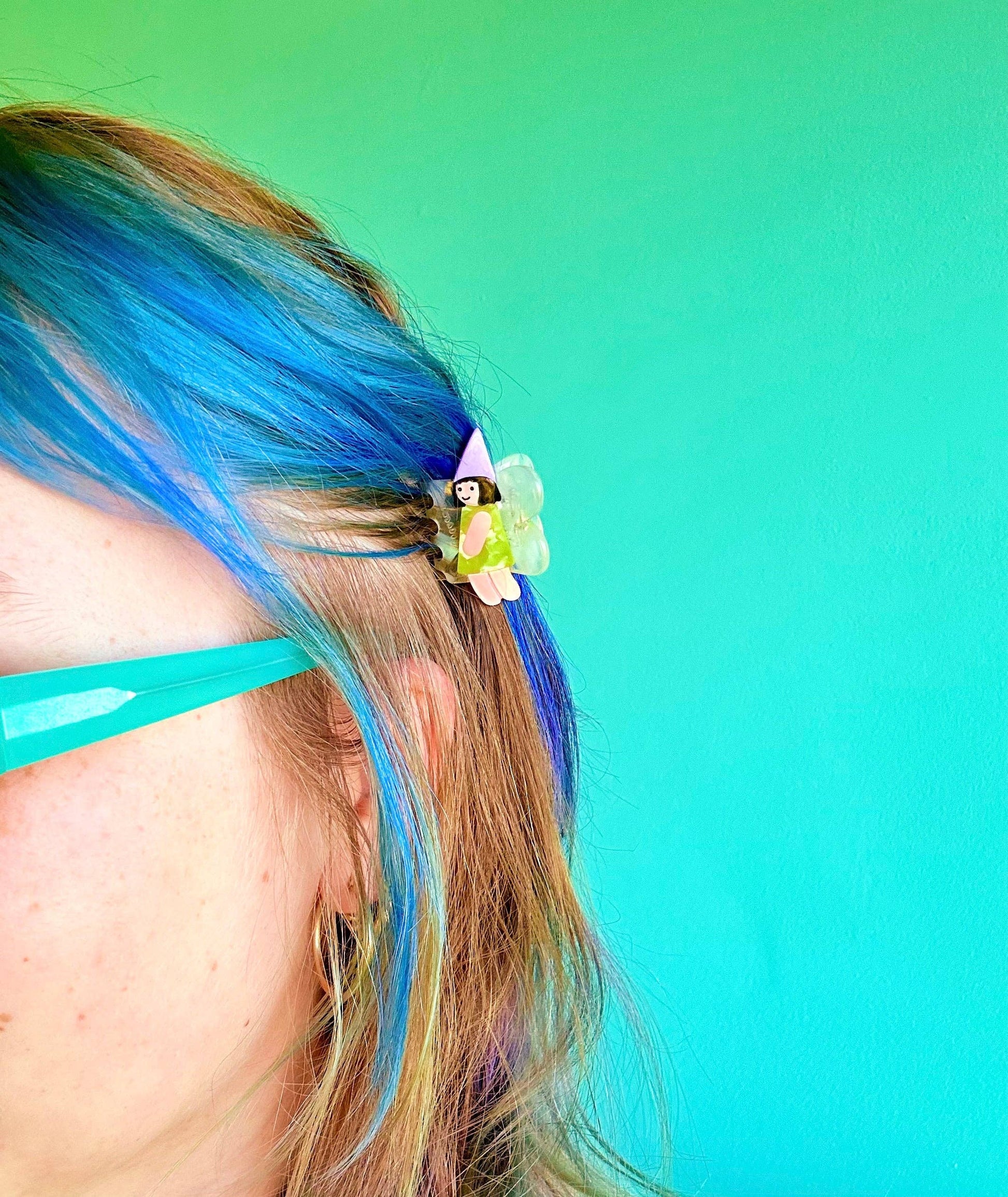 Person with blue hair and a decorative hair clip against a teal background
