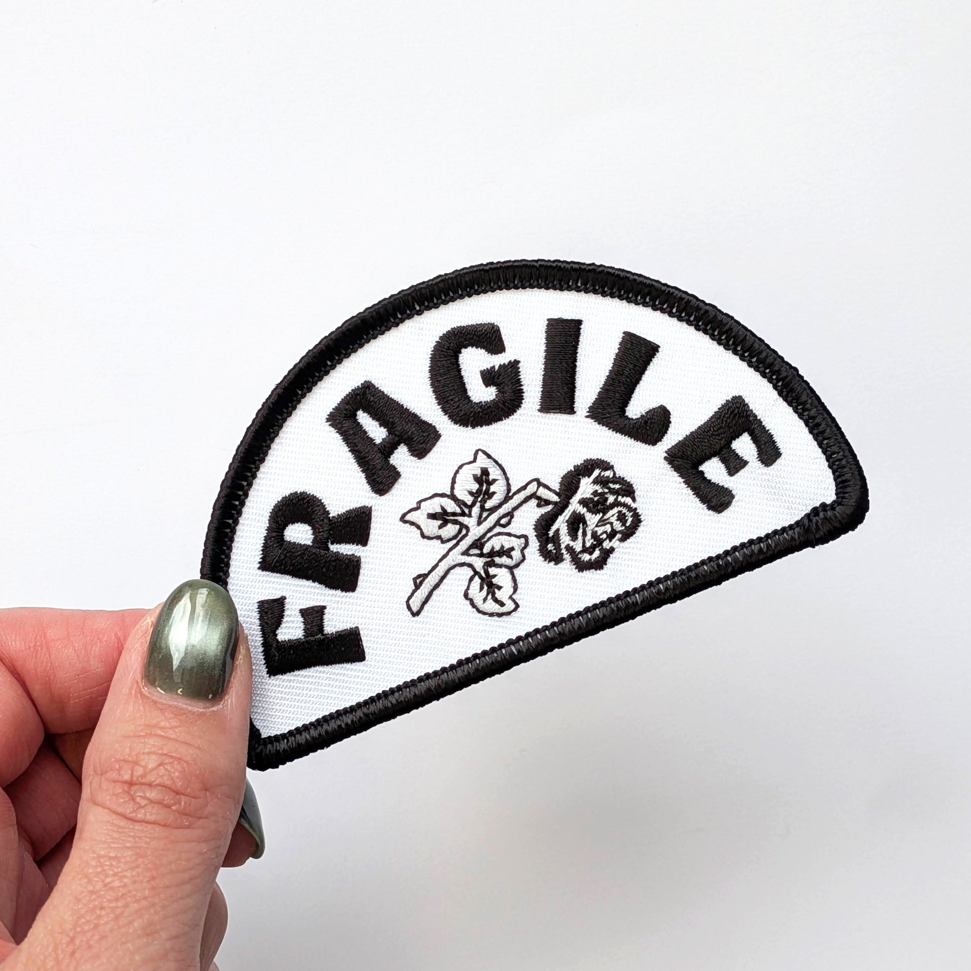 Patch with 'FRAGILE' text and a rose design held by a hand against a white background
