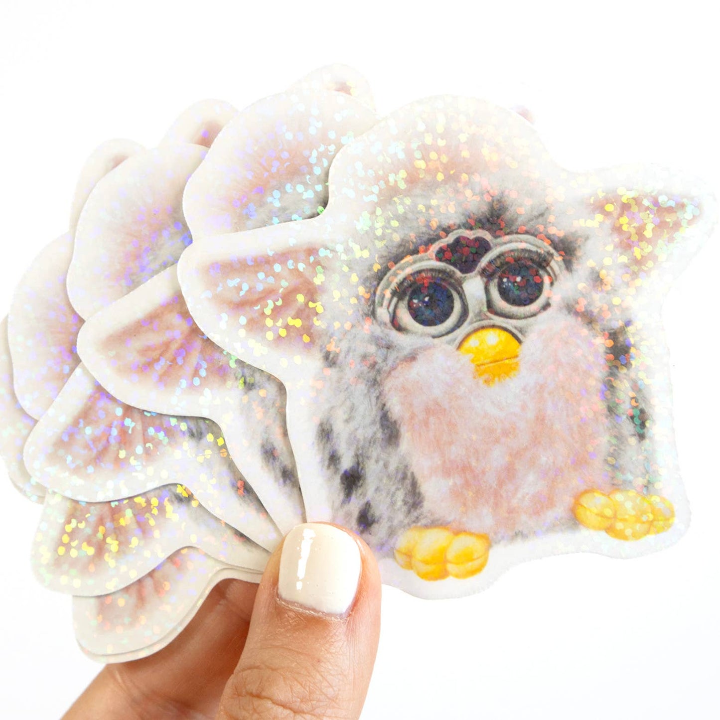 Hand holding a glittery furby sticker with a white background
