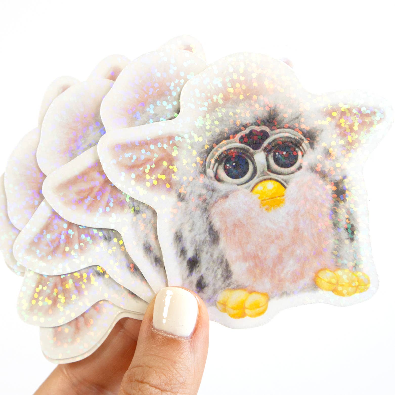 Hand holding a glittery furby sticker with a white background
