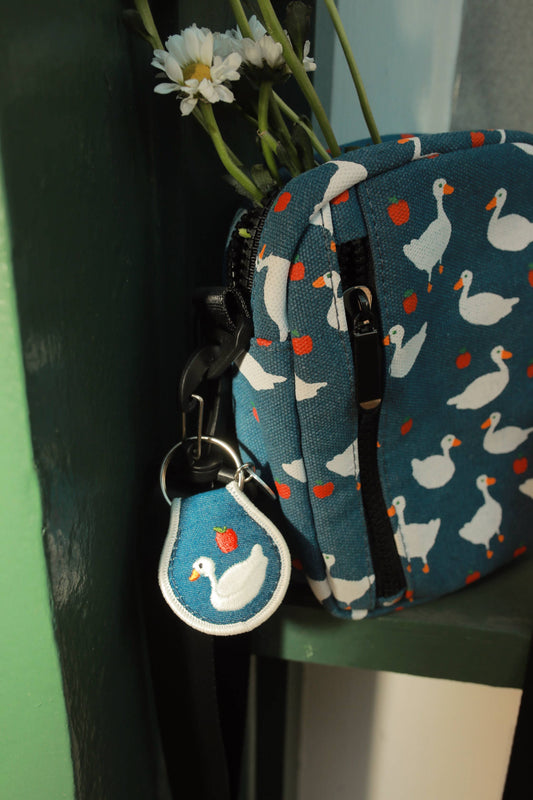 Small blue pouch with duck pattern and matching keychain on a green surface