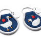 Two keychains with ducks and apples on a blue background