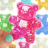 Pink glittery gummy bear sticker held by a hand with teal nail polish, colorful background.