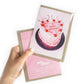 Hand holding a birthday card with a cake illustration and 'Happy Birthday!' text, brand 'Julia ockert' visible.
