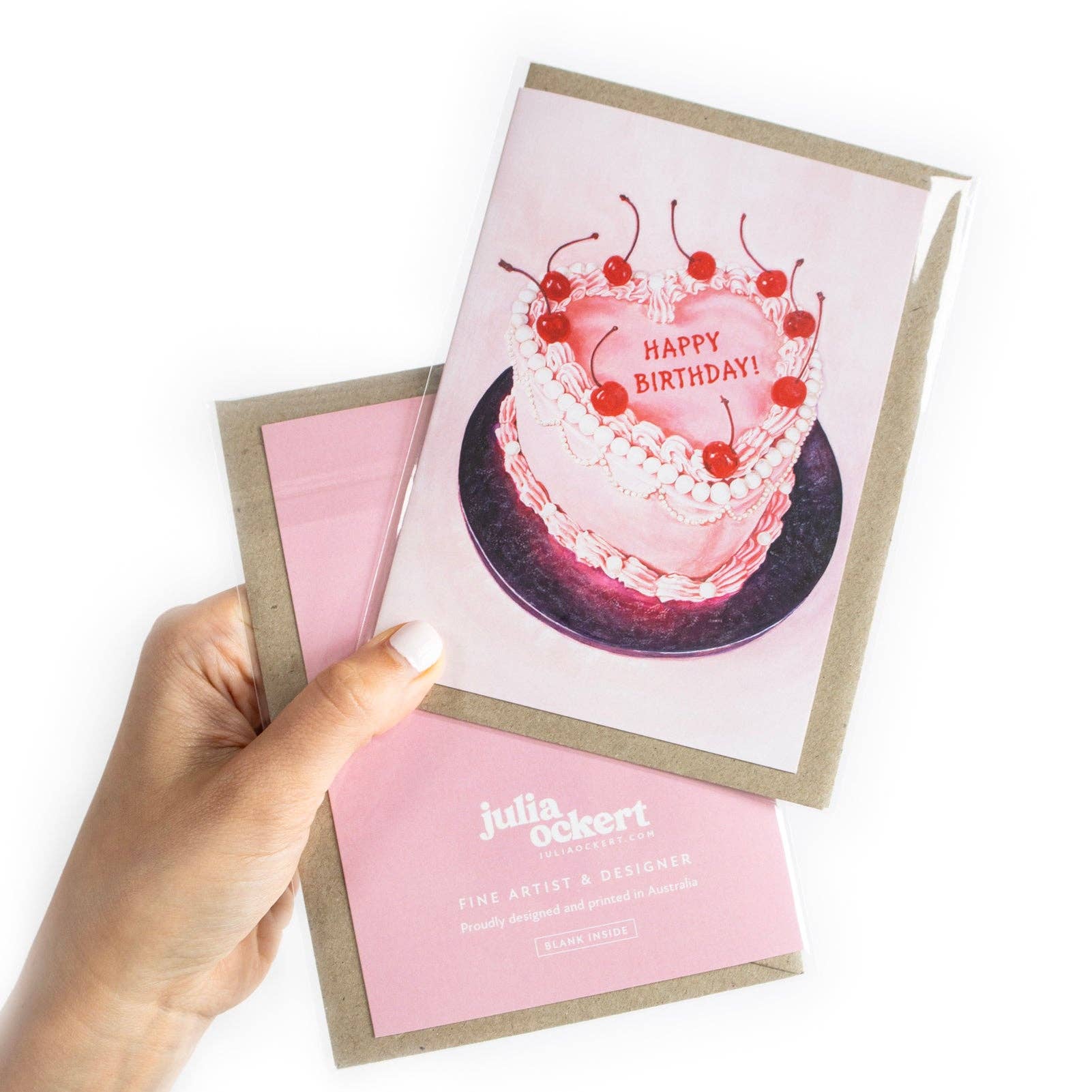 Hand holding a birthday card with a cake illustration and 'Happy Birthday!' text, brand 'Julia ockert' visible.