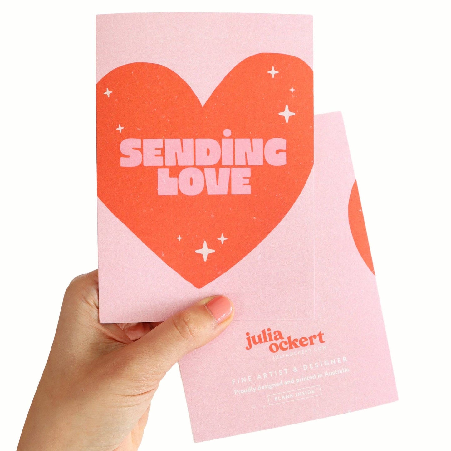 Pink card with a red heart and 'Sending Love' text held by a hand on a white background