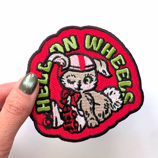 Embroidered patch with a bunny design and 'Hell on Wheels' text held by a hand.