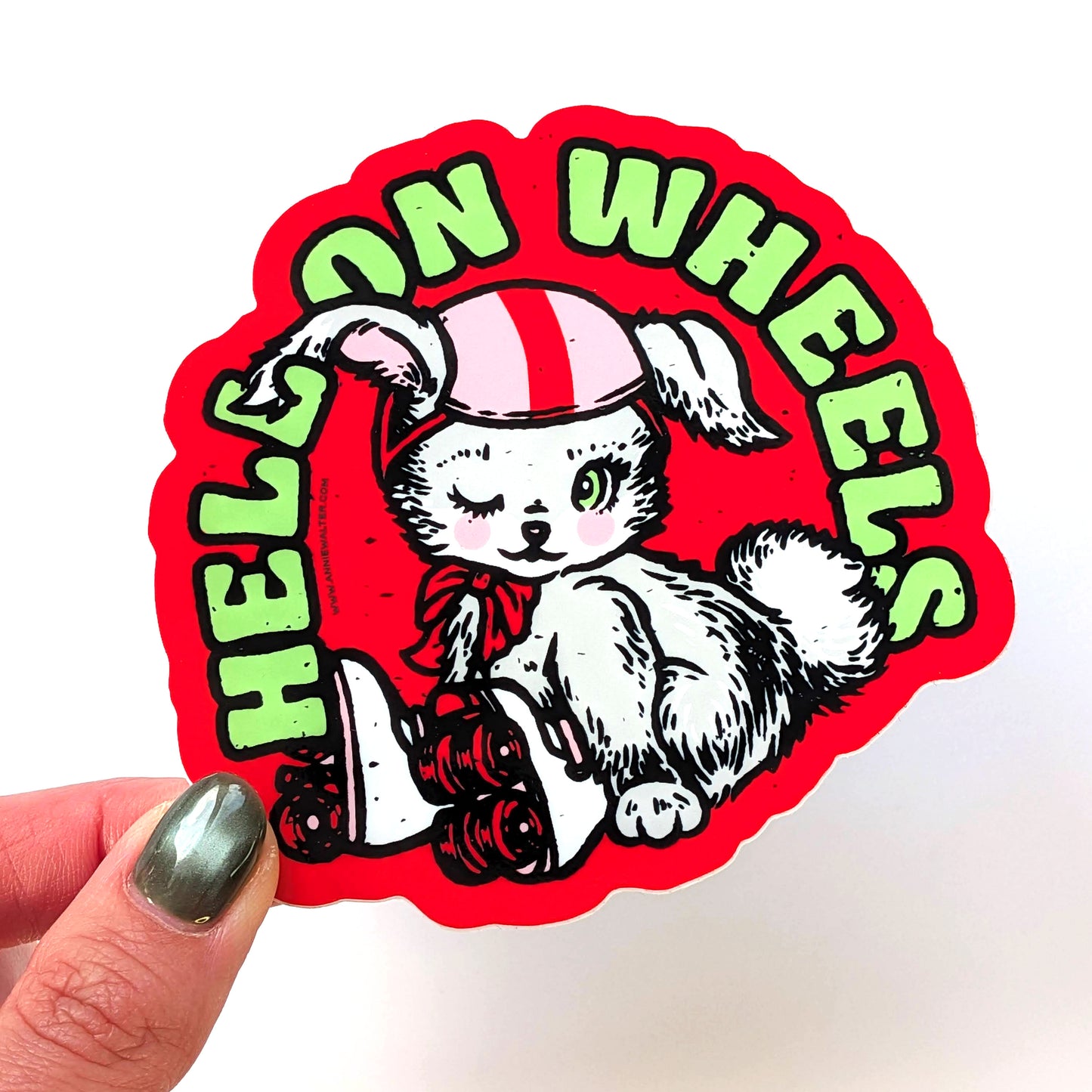 Sticker with a bunny on wheels design and 'HELL ON WHEELS' text held by a hand.