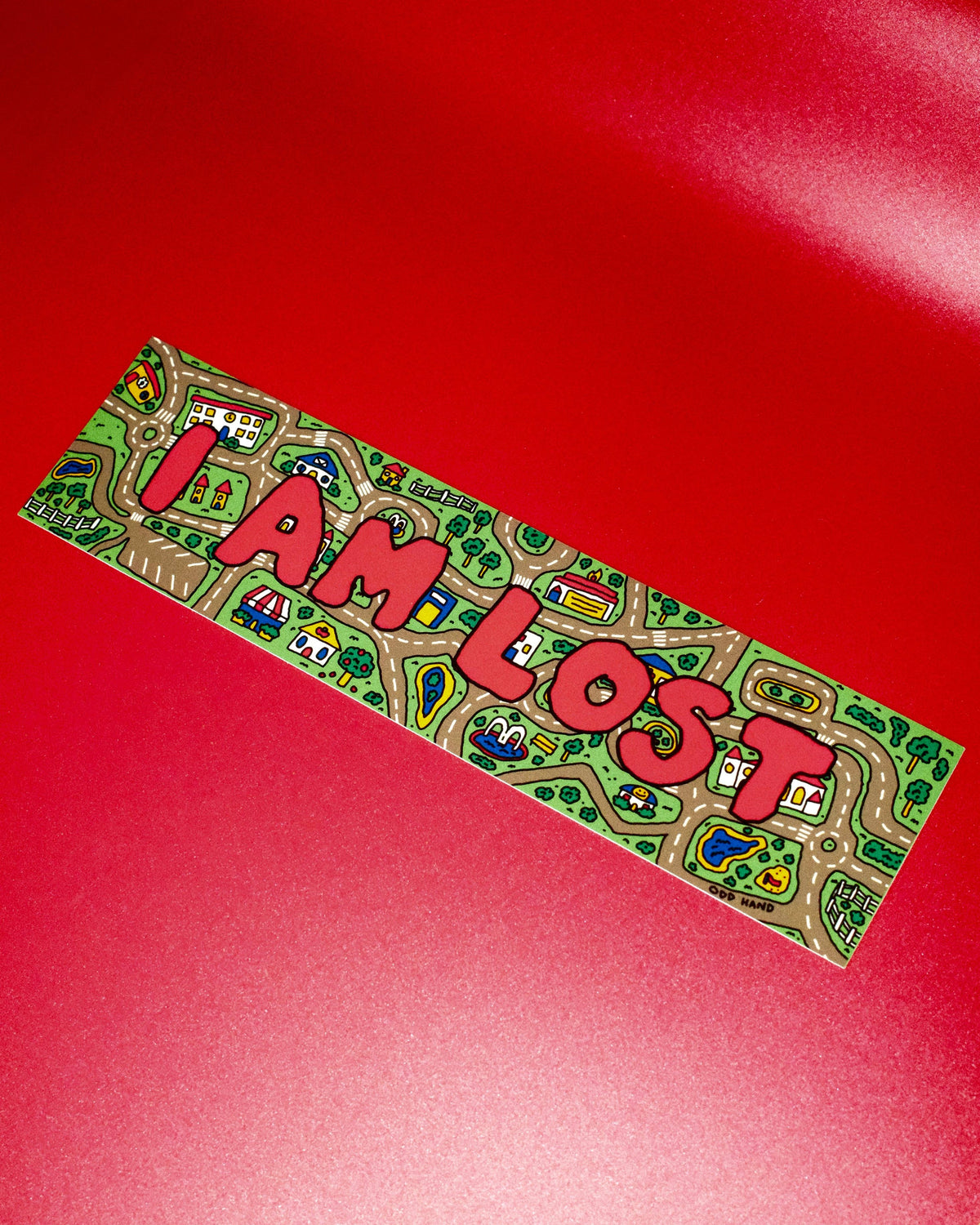 A rectangular sticker with a colorful cartoon map design and the words 'I AM LOST' in large red letters, placed diagonally on a solid red background.