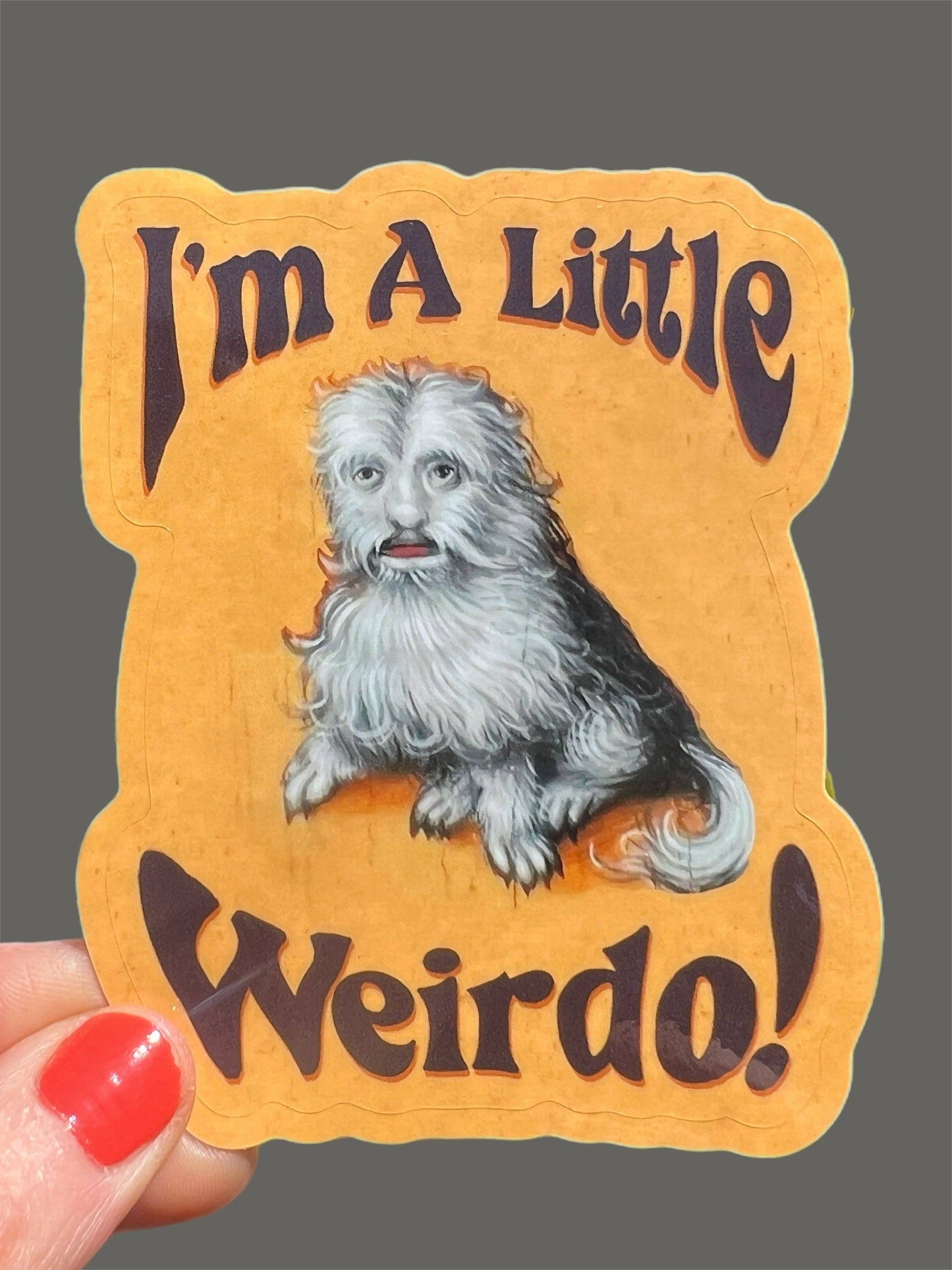 Sticker with a dog illustration and text 'I'm A Little Weirdo!' held by a hand.