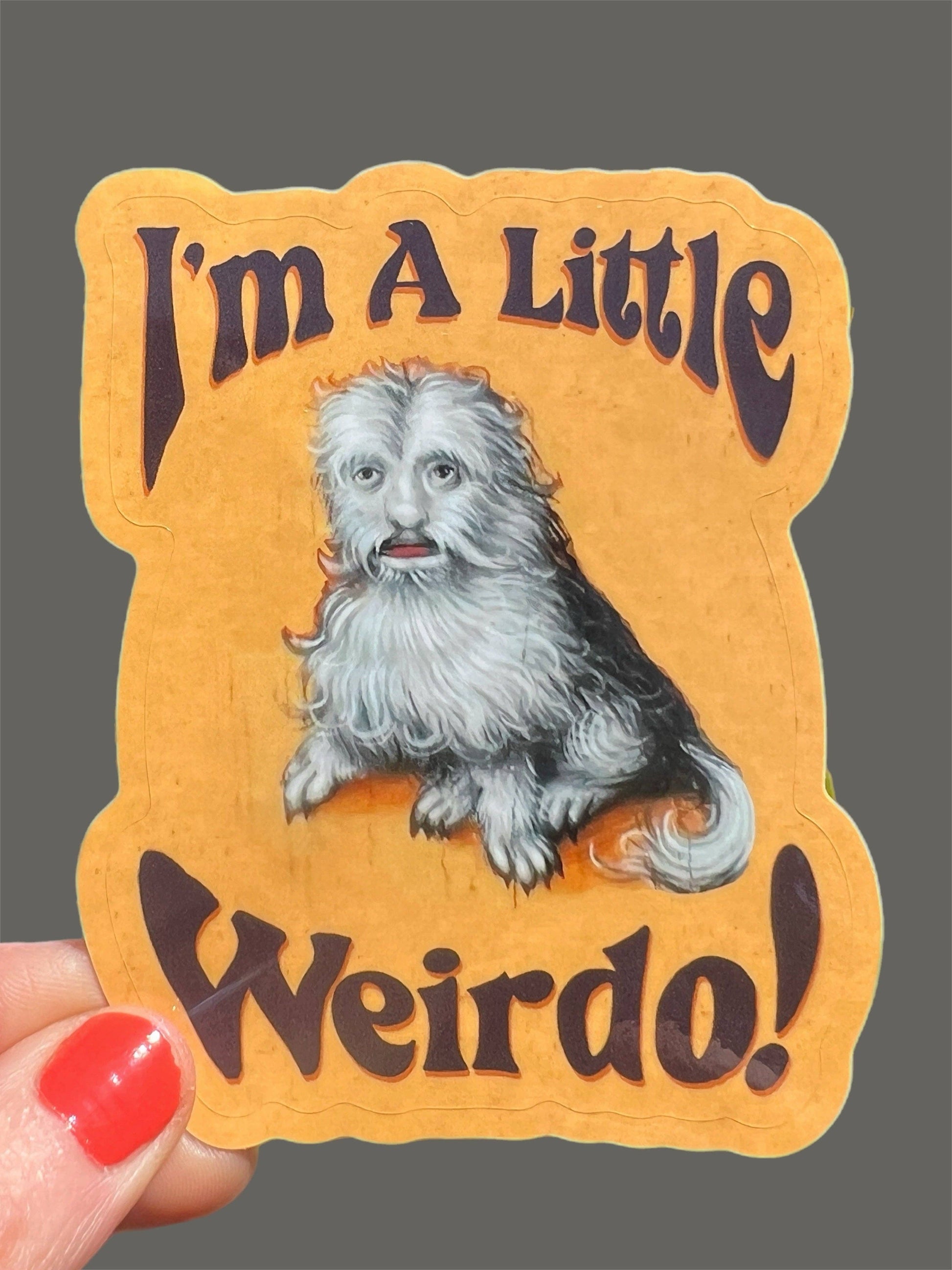 Sticker with a dog illustration and text 'I'm A Little Weirdo!' held by a hand.