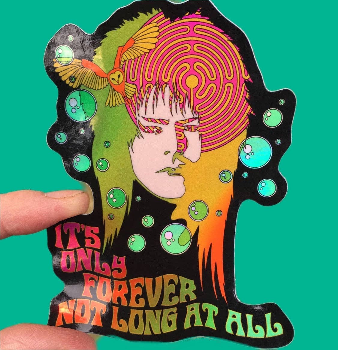 Colorful sticker with a stylized face and text 'It's only forever not long at all' held by a hand against a green background.
