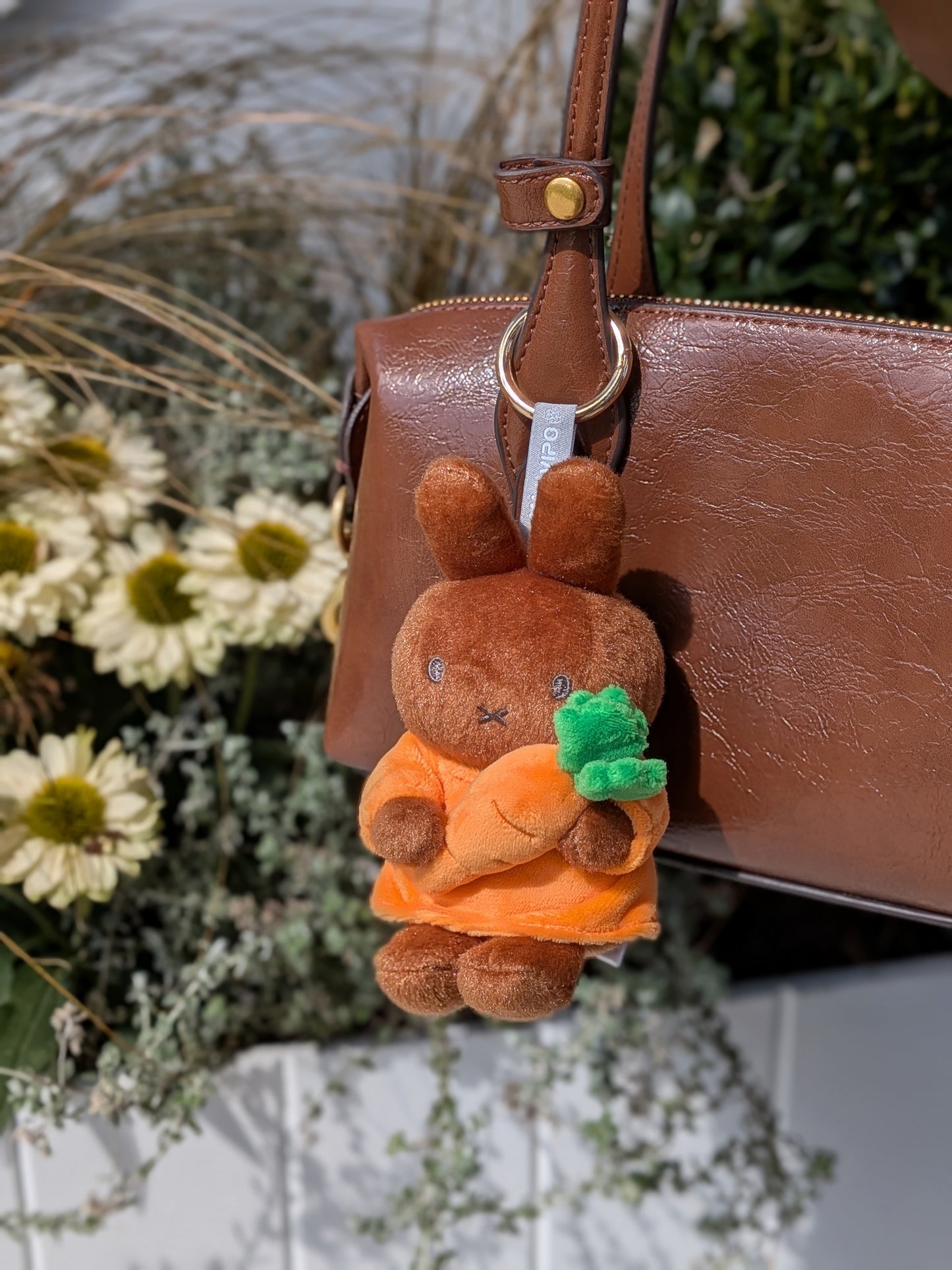 Plush keychain of Melanie holding a carrot attached to a brown handbag