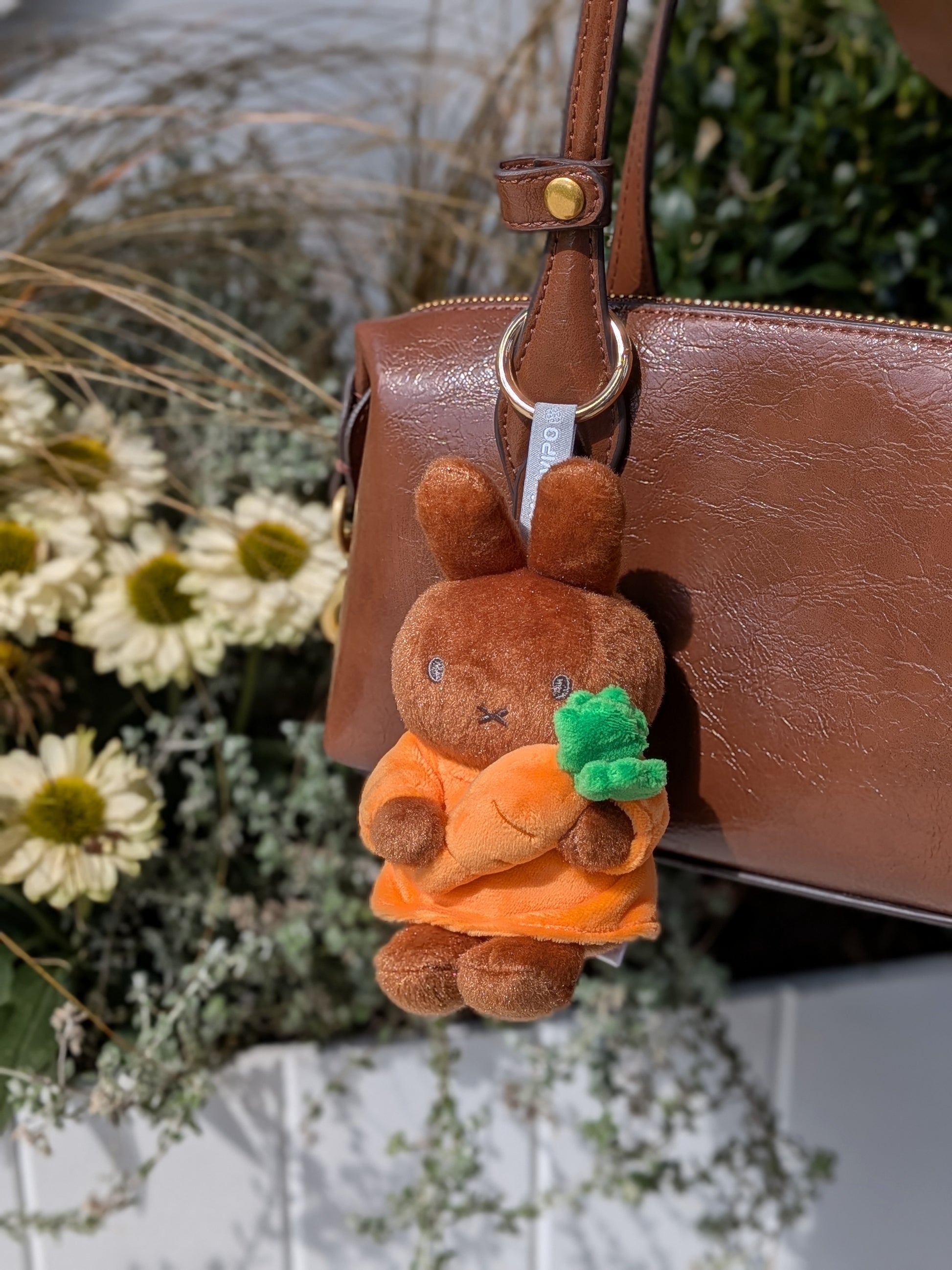 Plush keychain of Melanie holding a carrot attached to a brown handbag