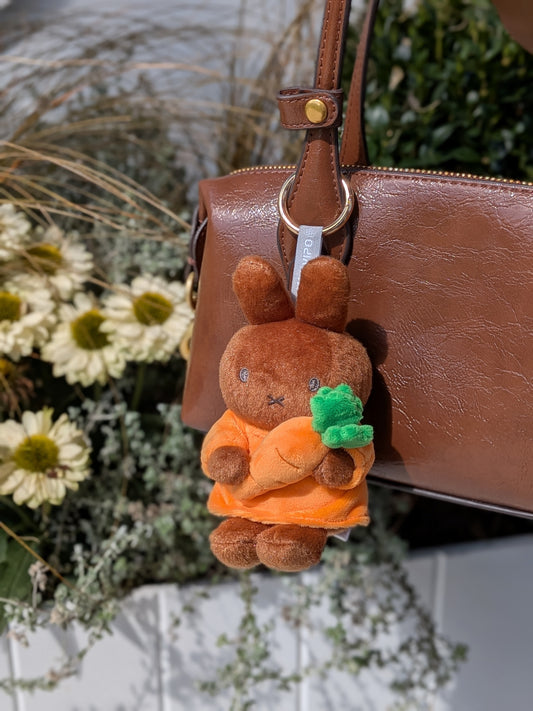 Plush keychain of Melanie holding a carrot attached to a brown handbag