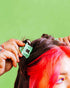 Person with red hair getting a green hair dyeputting a hair lip to their hair against a green background