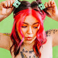 Person with pink hair and tattoos adjusting hair clips against a green background