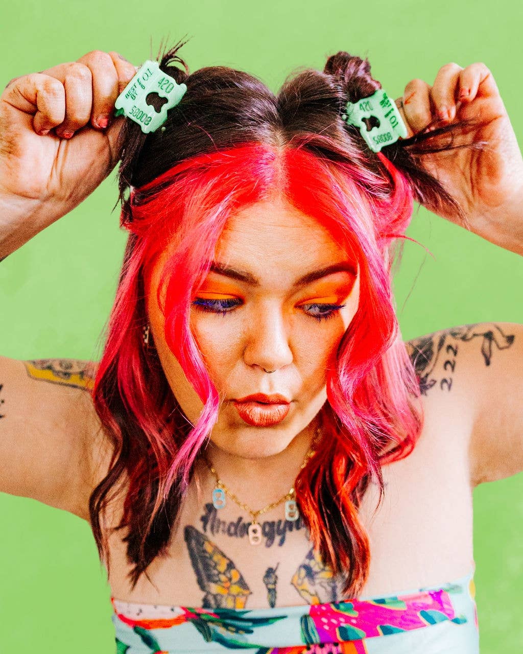 Person with pink hair and tattoos adjusting hair clips against a green background