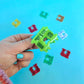 Hand holding a green hair clip with numbers against a blue background with colorful shapes.