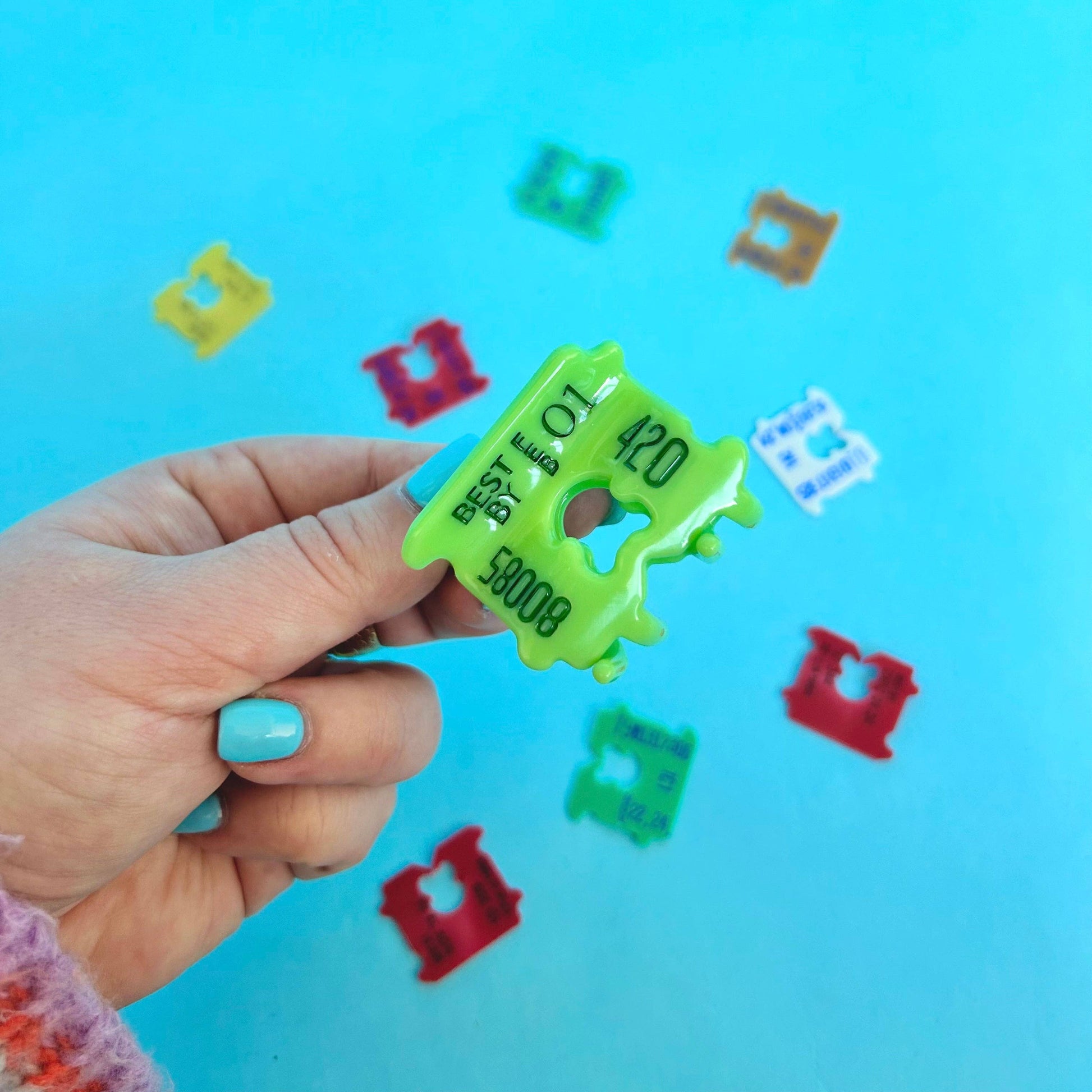 Hand holding a green hair clip with numbers against a blue background with colorful shapes.