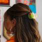 Person with a colorful hair clip in an indoor setting with artwork on the wall.