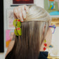 Person with blonde hair wearing two olive hair clips