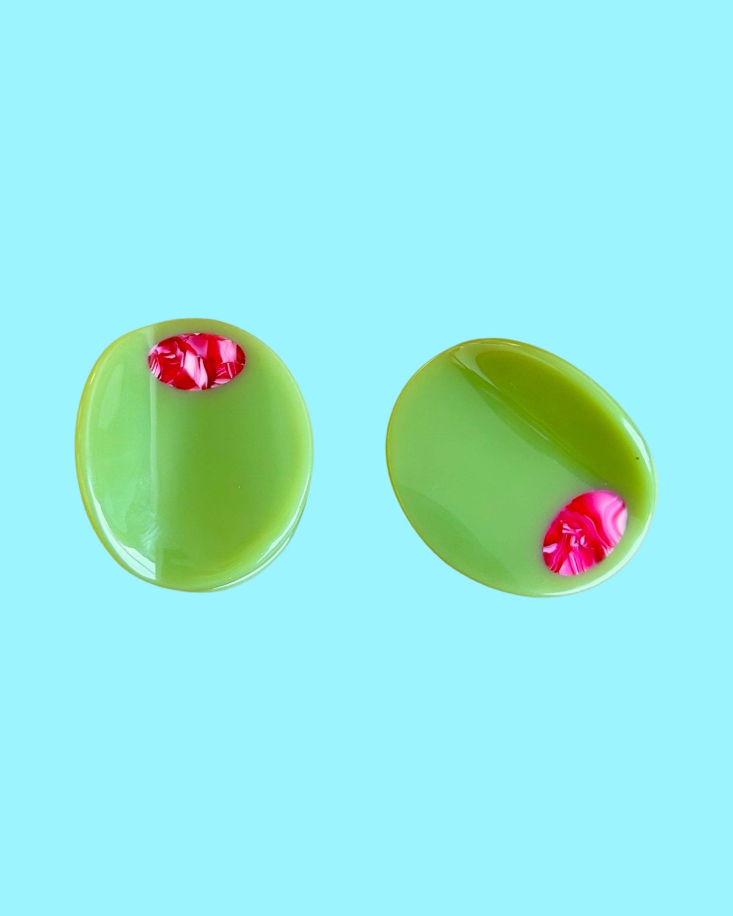 Two green olive hair clips with red centers on a light blue background