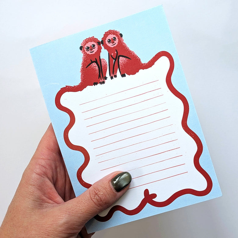 Hand holding a blue notepad with a monkey design